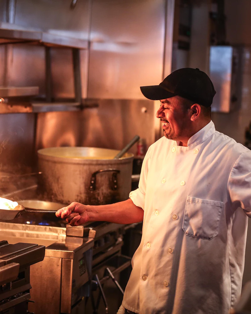 Chef in a white double-breasted chef jacket working on a commercial kitchen line